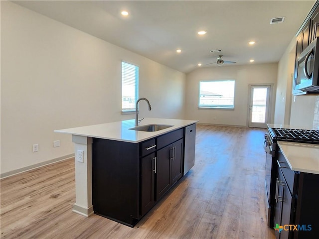 kitchen with sink, ceiling fan, stainless steel appliances, light hardwood / wood-style floors, and a center island with sink