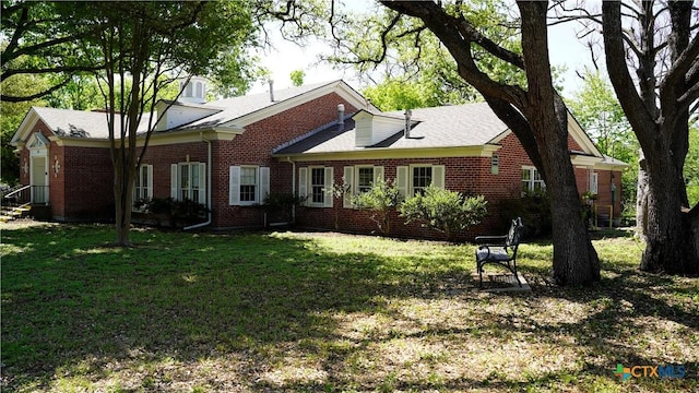 back of house featuring brick siding and a lawn