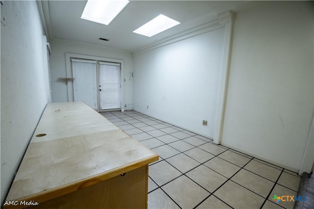 tiled empty room with ornamental molding and a skylight