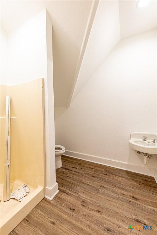 204 Ave F, Shiner, TX 77984 - full bathroom with a stall shower, vaulted ceiling, baseboards, toilet, and wood finished floors