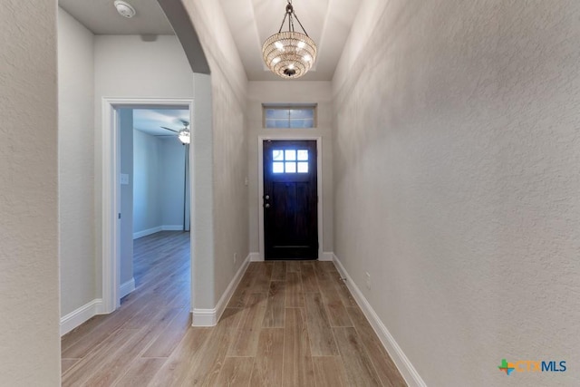 foyer entrance with ceiling fan with notable chandelier, light wood-type flooring, and a towering ceiling