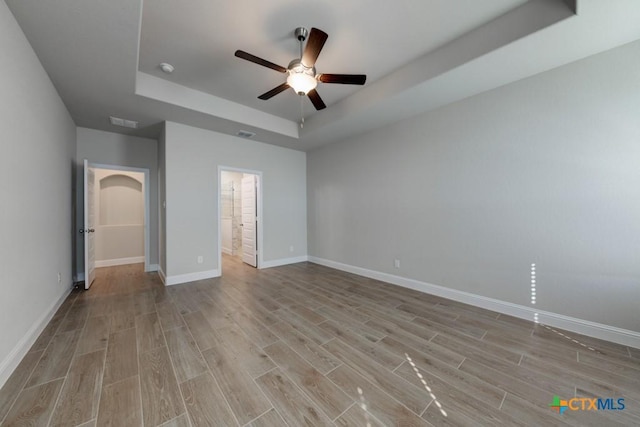 unfurnished bedroom featuring ceiling fan, light hardwood / wood-style floors, a tray ceiling, and ensuite bath