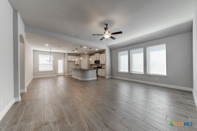 unfurnished living room with ceiling fan with notable chandelier, sink, and light hardwood / wood-style flooring