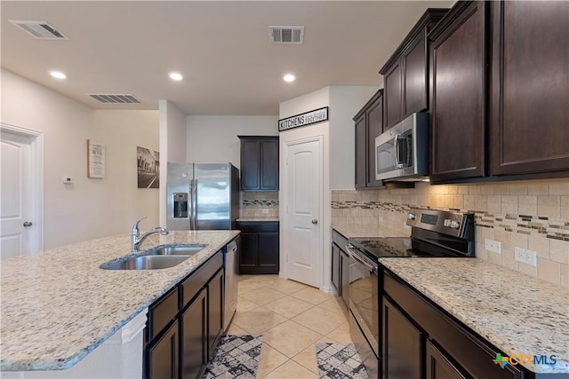 kitchen with stainless steel appliances, sink, a kitchen island with sink, and light stone counters