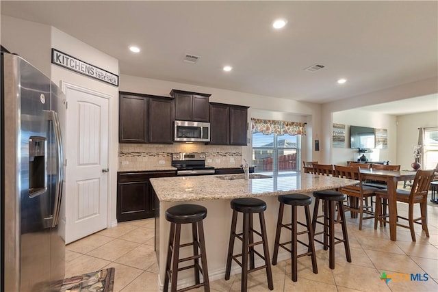 kitchen with dark brown cabinetry, sink, a center island with sink, a kitchen breakfast bar, and stainless steel appliances