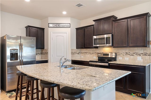 kitchen featuring sink, a center island with sink, light tile patterned floors, appliances with stainless steel finishes, and light stone countertops