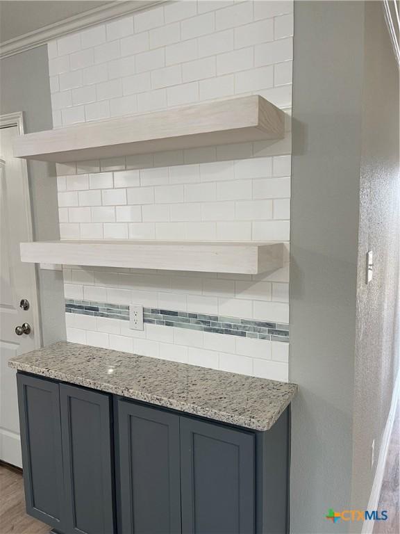 kitchen featuring gray cabinets, tasteful backsplash, light stone counters, and hardwood / wood-style flooring