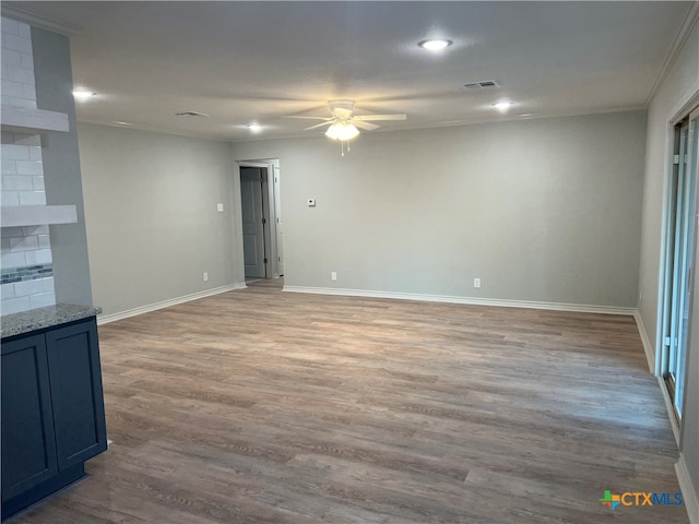 empty room featuring ceiling fan, a fireplace, light wood-type flooring, and crown molding