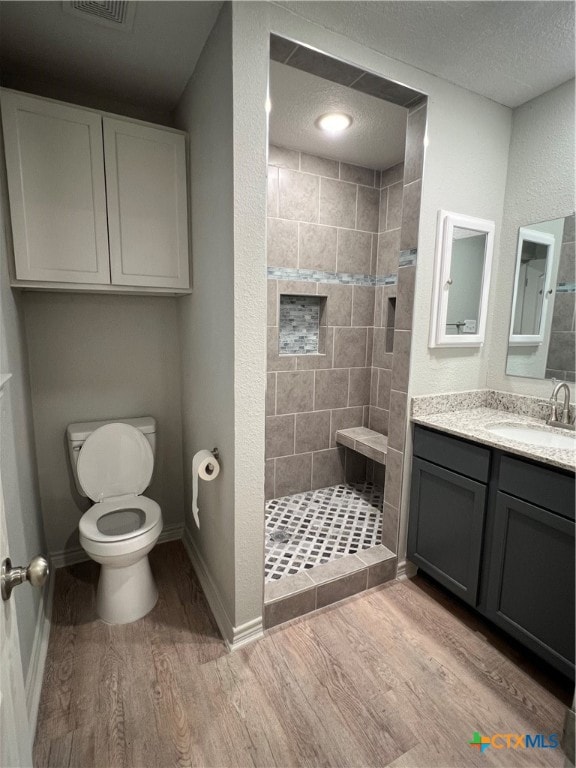 bathroom with hardwood / wood-style floors, vanity, toilet, a textured ceiling, and a tile shower