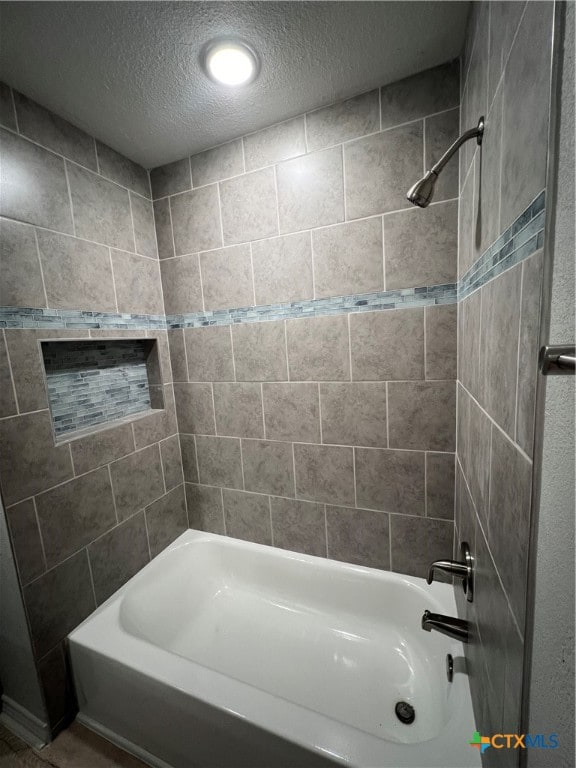 bathroom with a textured ceiling and tiled shower / bath combo