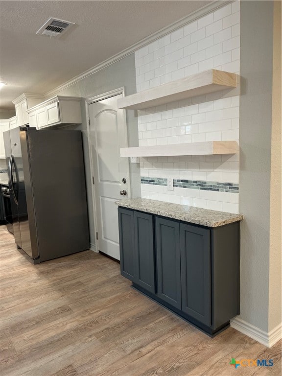 kitchen featuring backsplash, stainless steel refrigerator, light stone countertops, and light wood-type flooring