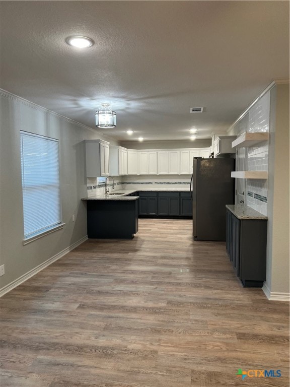 kitchen with white cabinets, light hardwood / wood-style flooring, fridge, and ornamental molding