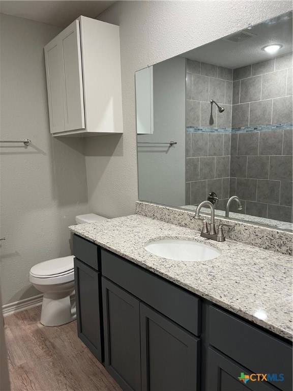 bathroom featuring vanity, toilet, wood-type flooring, and a tile shower