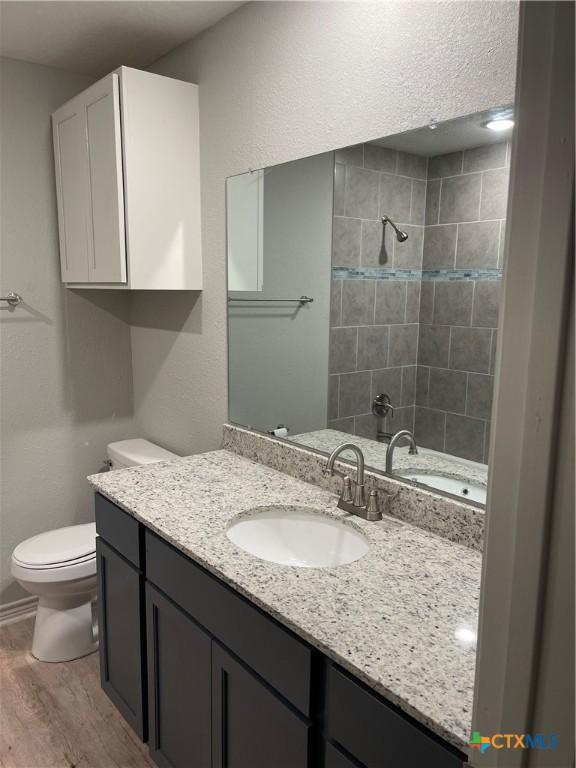 bathroom featuring hardwood / wood-style floors, vanity, a tile shower, and toilet