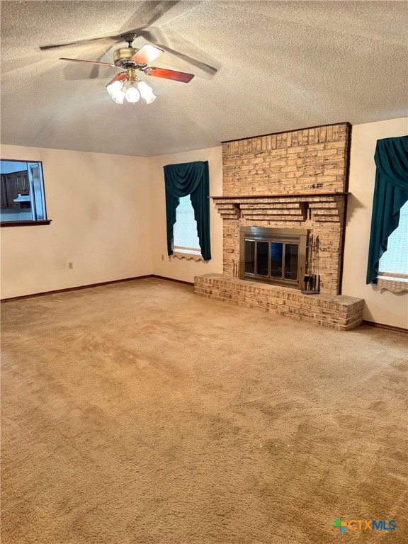 unfurnished living room featuring ceiling fan, carpet floors, a textured ceiling, and a brick fireplace