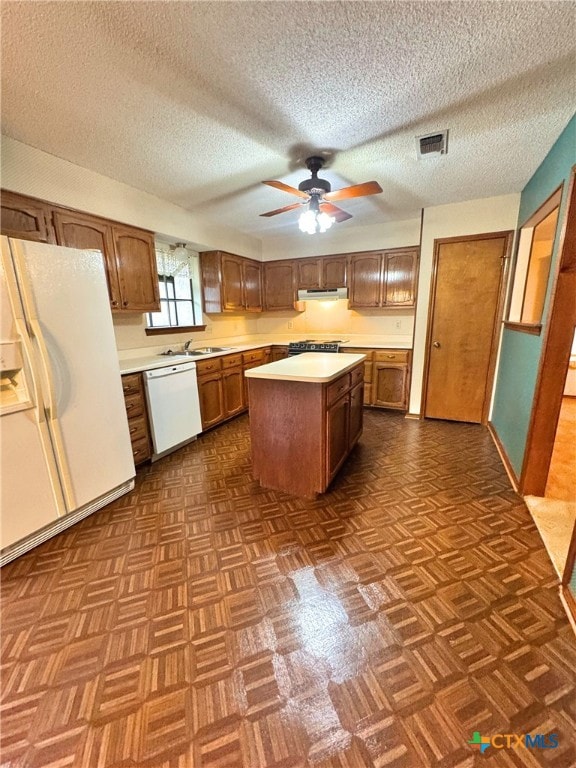 kitchen featuring a textured ceiling, ceiling fan, a center island, and white appliances