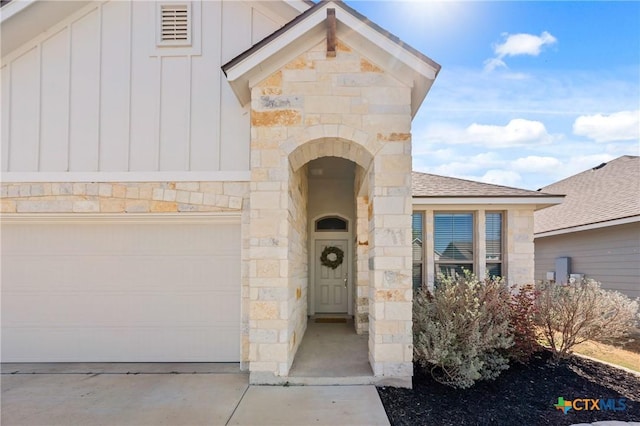 view of exterior entry featuring stone siding, concrete driveway, board and batten siding, a shingled roof, and visible vents