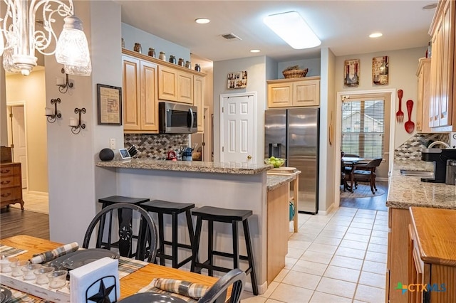 kitchen featuring light tile patterned flooring, appliances with stainless steel finishes, decorative light fixtures, backsplash, and light stone counters