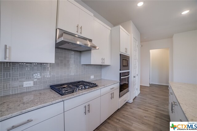 kitchen featuring tasteful backsplash, appliances with stainless steel finishes, light stone countertops, white cabinets, and light hardwood / wood-style flooring