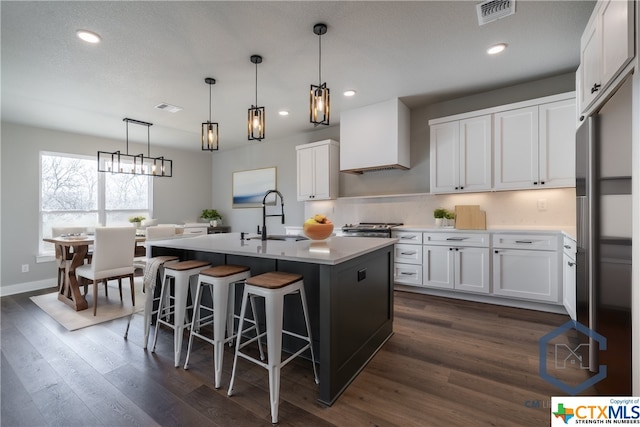 kitchen with dark hardwood / wood-style flooring, a kitchen island with sink, sink, pendant lighting, and white cabinets