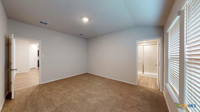 unfurnished bedroom featuring lofted ceiling, light carpet, and ensuite bathroom