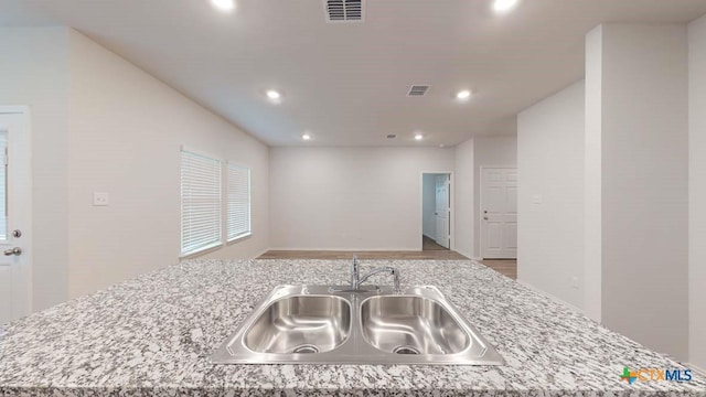 kitchen featuring light stone counters, sink, light hardwood / wood-style floors, and a center island with sink