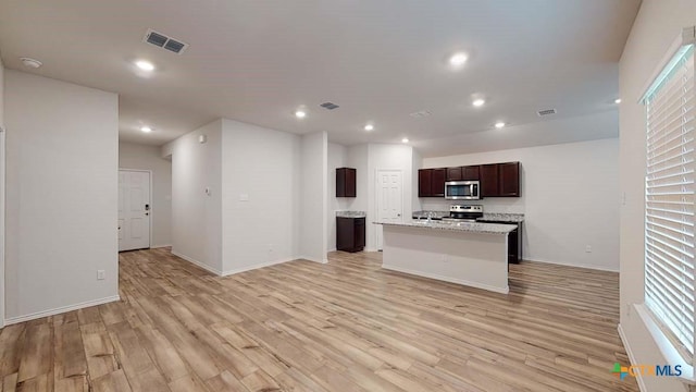 kitchen featuring light stone countertops, an island with sink, appliances with stainless steel finishes, and light wood-type flooring