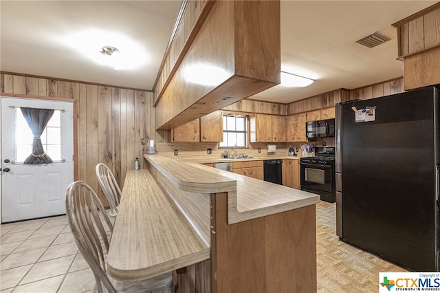 kitchen featuring sink, a breakfast bar, black appliances, kitchen peninsula, and wood walls