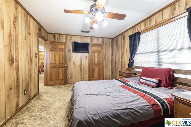 carpeted bedroom with crown molding, wooden walls, and ceiling fan