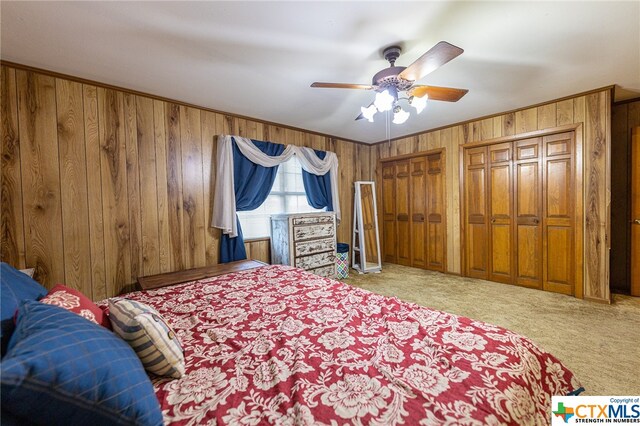 bedroom featuring two closets, light carpet, ceiling fan, and wood walls