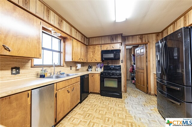 kitchen with sink, black appliances, and wood walls