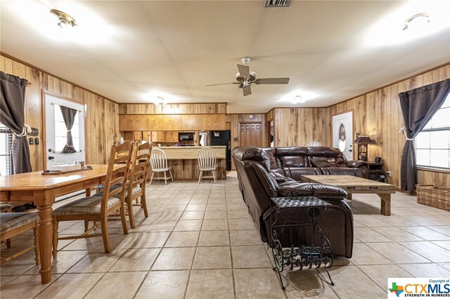 living room with ceiling fan, wooden walls, and light tile patterned floors