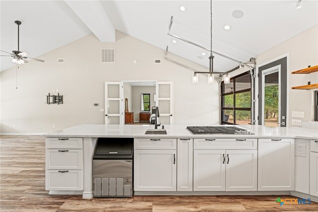 kitchen with white cabinetry, sink, stainless steel gas stovetop, vaulted ceiling with beams, and light hardwood / wood-style flooring