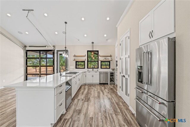 kitchen with beverage cooler, light hardwood / wood-style flooring, hanging light fixtures, white cabinetry, and appliances with stainless steel finishes