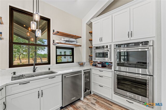 kitchen with stainless steel appliances, light wood-type flooring, white cabinetry, sink, and vaulted ceiling