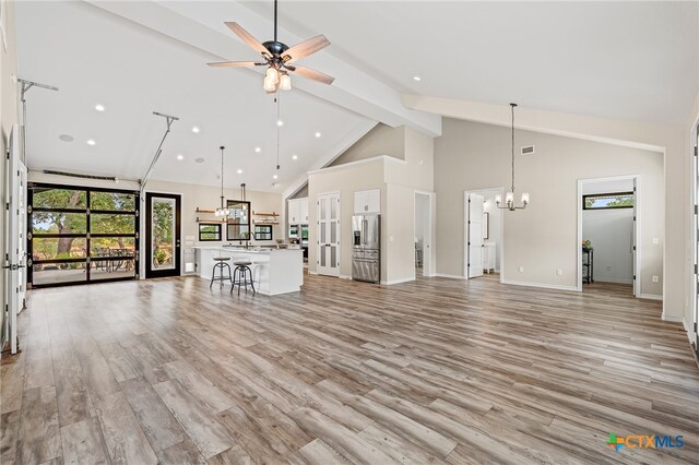 unfurnished living room featuring high vaulted ceiling, sink, light hardwood / wood-style floors, and ceiling fan with notable chandelier