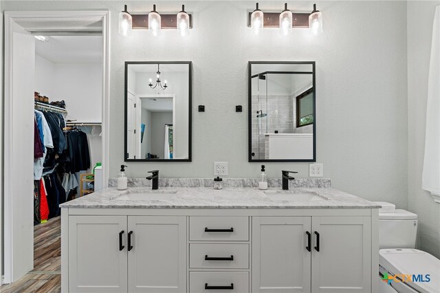 bathroom featuring a shower with door, an inviting chandelier, hardwood / wood-style floors, vanity, and toilet