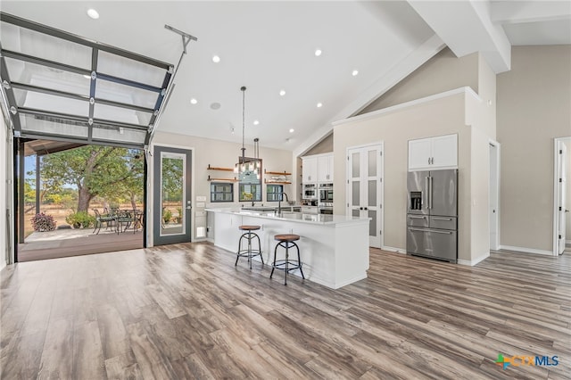 kitchen with a large island with sink, high vaulted ceiling, white cabinets, pendant lighting, and high end fridge