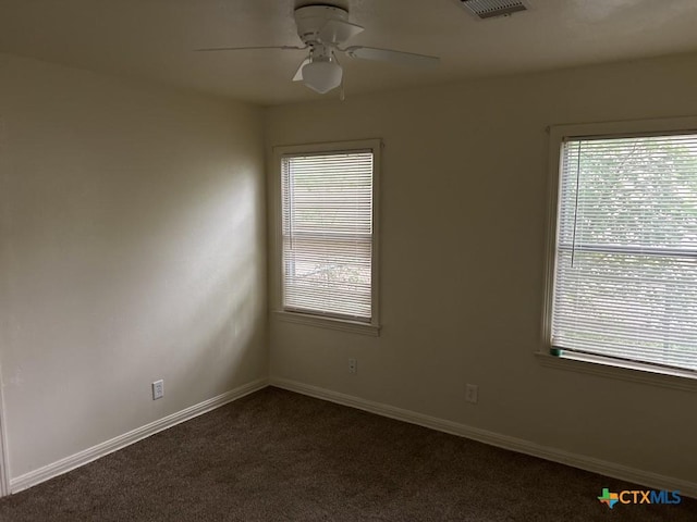 spare room featuring dark colored carpet, baseboards, visible vents, and ceiling fan