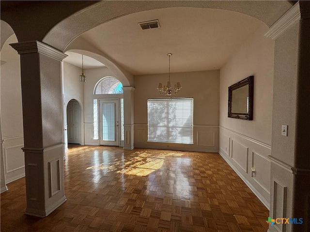 entrance foyer featuring dark parquet flooring, decorative columns, and an inviting chandelier