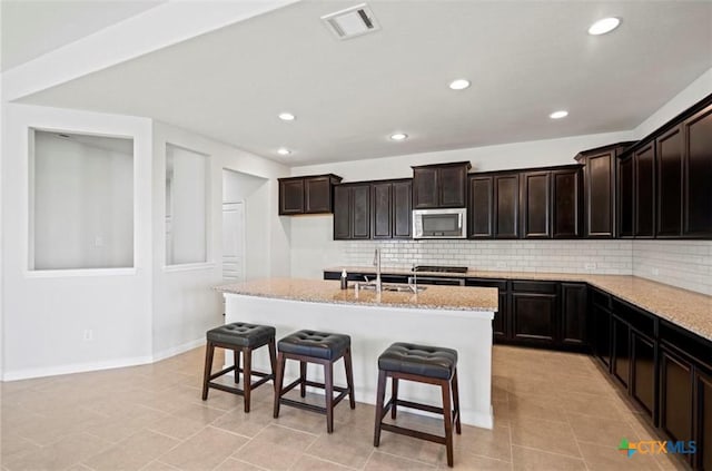 30125 Prairie Creek Ct, Brookshire, TX 77423 - kitchen with stainless steel microwave, light stone countertops, tasteful backsplash, recessed lighting, and a breakfast bar area