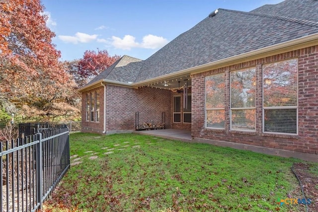 rear view of house featuring a yard, a fenced backyard, brick siding, and roof with shingles