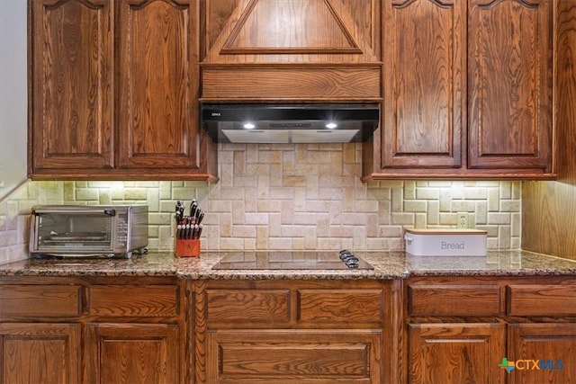 kitchen featuring black electric stovetop, ventilation hood, a toaster, and tasteful backsplash