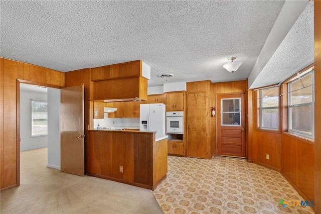 kitchen with white appliances, wooden walls, kitchen peninsula, and a wealth of natural light