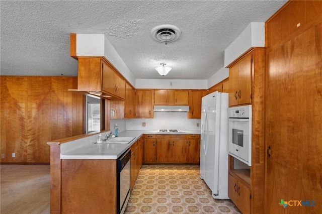 kitchen with wooden walls, sink, white appliances, kitchen peninsula, and a textured ceiling