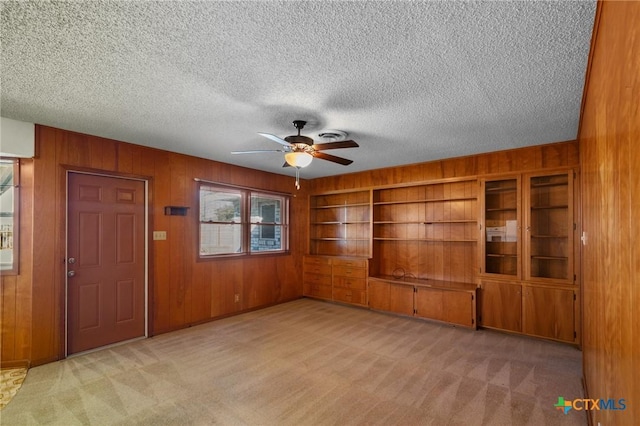 unfurnished living room with light colored carpet, a textured ceiling, and wood walls