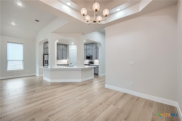 kitchen with an island with sink, a tray ceiling, a chandelier, refrigerator, and light hardwood / wood-style flooring