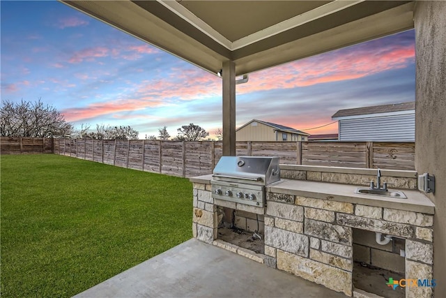 patio terrace at dusk with a yard, an outdoor kitchen, area for grilling, and sink