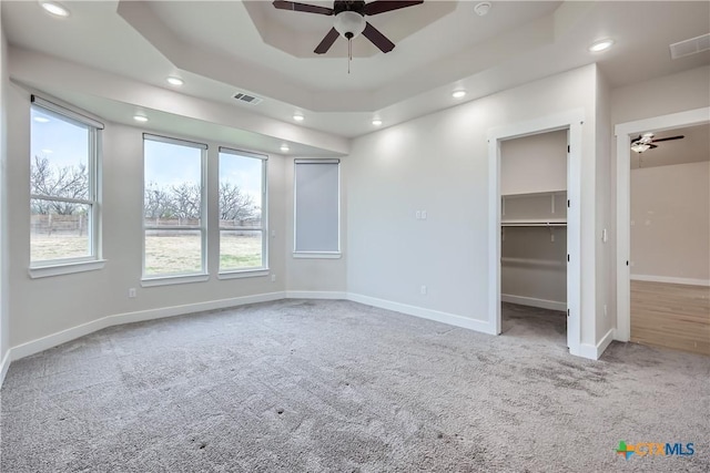 empty room with ceiling fan, carpet, a raised ceiling, and a healthy amount of sunlight