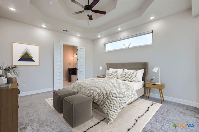 carpeted bedroom featuring ceiling fan, ensuite bathroom, and a raised ceiling